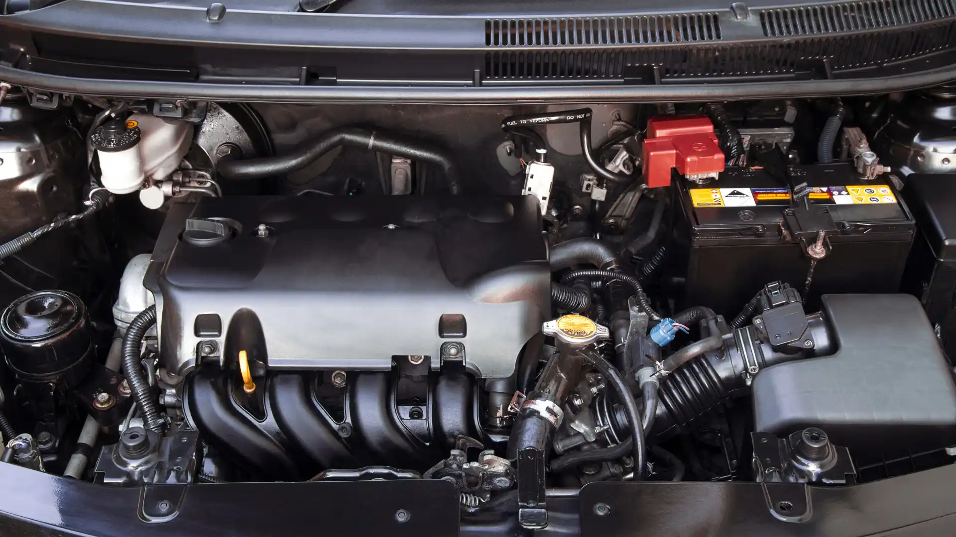 A close-up view of a car engine bay showcasing various components, including the engine block, battery, and fluid reservoirs, with clean and organized wiring.


